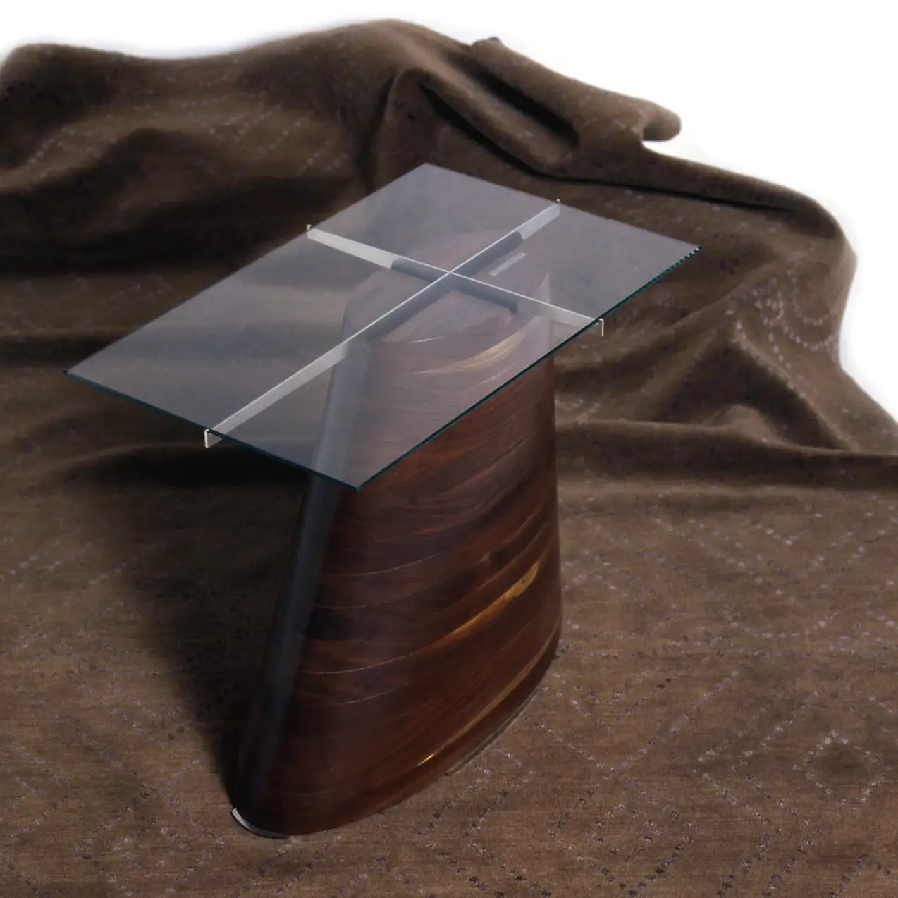Trunk Table photographed against draped brown fabric, highlighting its tapered walnut base and glass top.